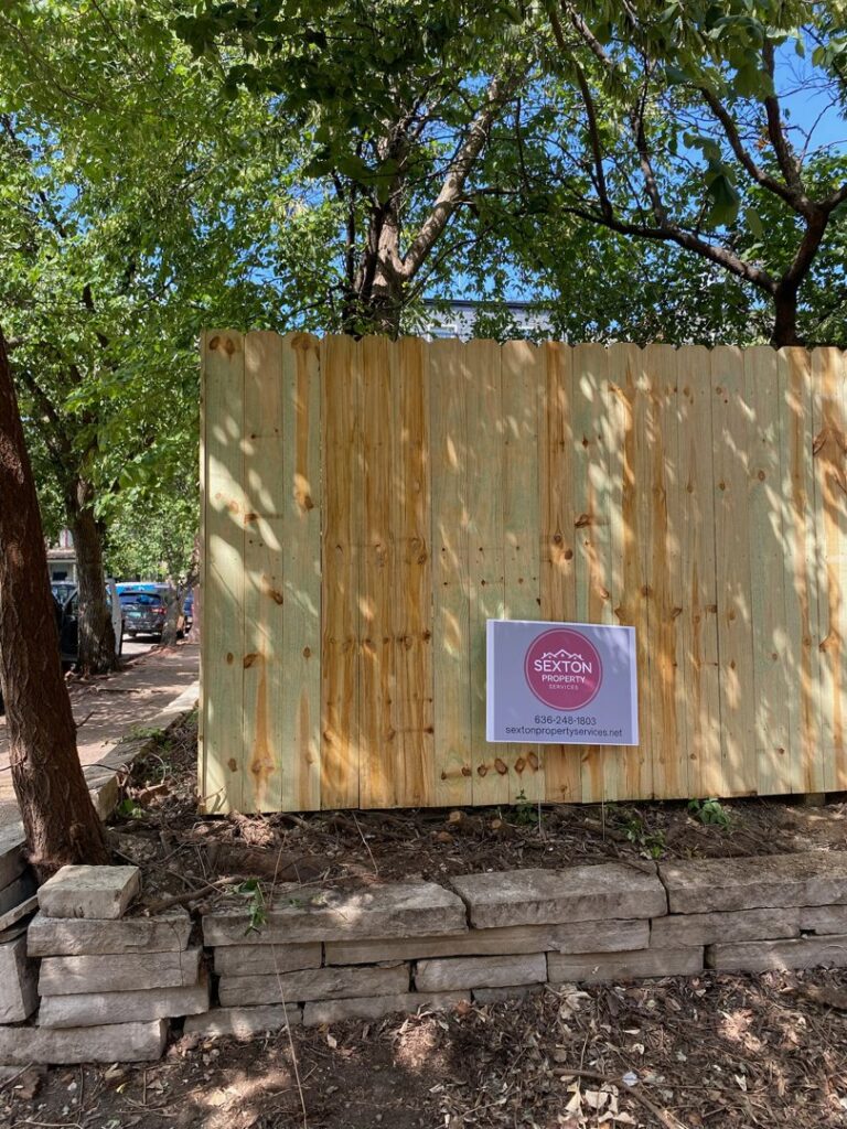 A newly installed wood privacy fence with a business sign by Sexton Property Services STL in High Ridge, MO.
