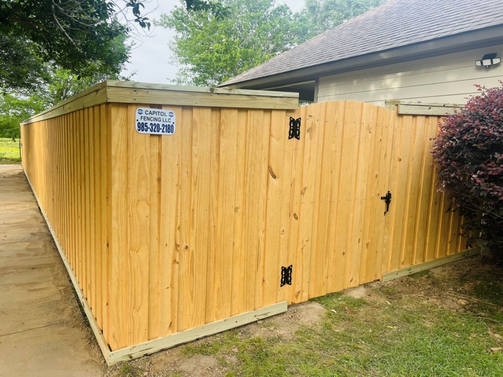 A newly installed wooden privacy fence featuring a curved top gate next to a residential home by Capitol Fencing in Baton Rouge, LA.