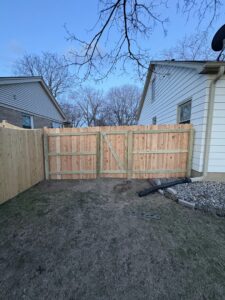 A newly installed natural wood privacy fence with a double gate in a residential backyard by Safe Yard Fence - Waukesha County in Waukesha, WI.