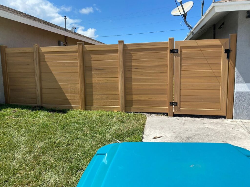 A newly installed wood privacy fence with a gate in a residential backyard by Palm's Fence of Miami, FL.