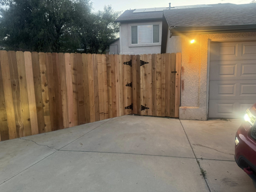 A newly installed wood privacy fence with a gate leading to a driveway by HG Fencing LLC in Fountain, CO.