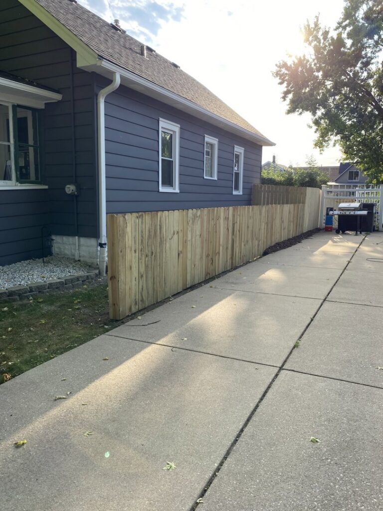 A newly installed natural wood privacy fence with a gate next to a residential house by Safe Yard Fence - Waukesha County in Waukesha, WI.