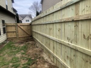 A newly installed wood privacy fence with a gate next to a residential home by Right Now Fencing, LLC in Johns Creek, GA