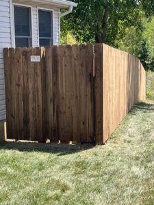 A newly installed wood privacy fence with a gate next to a house by Sexton Property Services STL in High Ridge, MO.