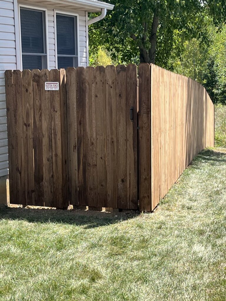 A newly installed wood privacy fence with a gate next to a house by Sexton Property Services STL in High Ridge, MO.