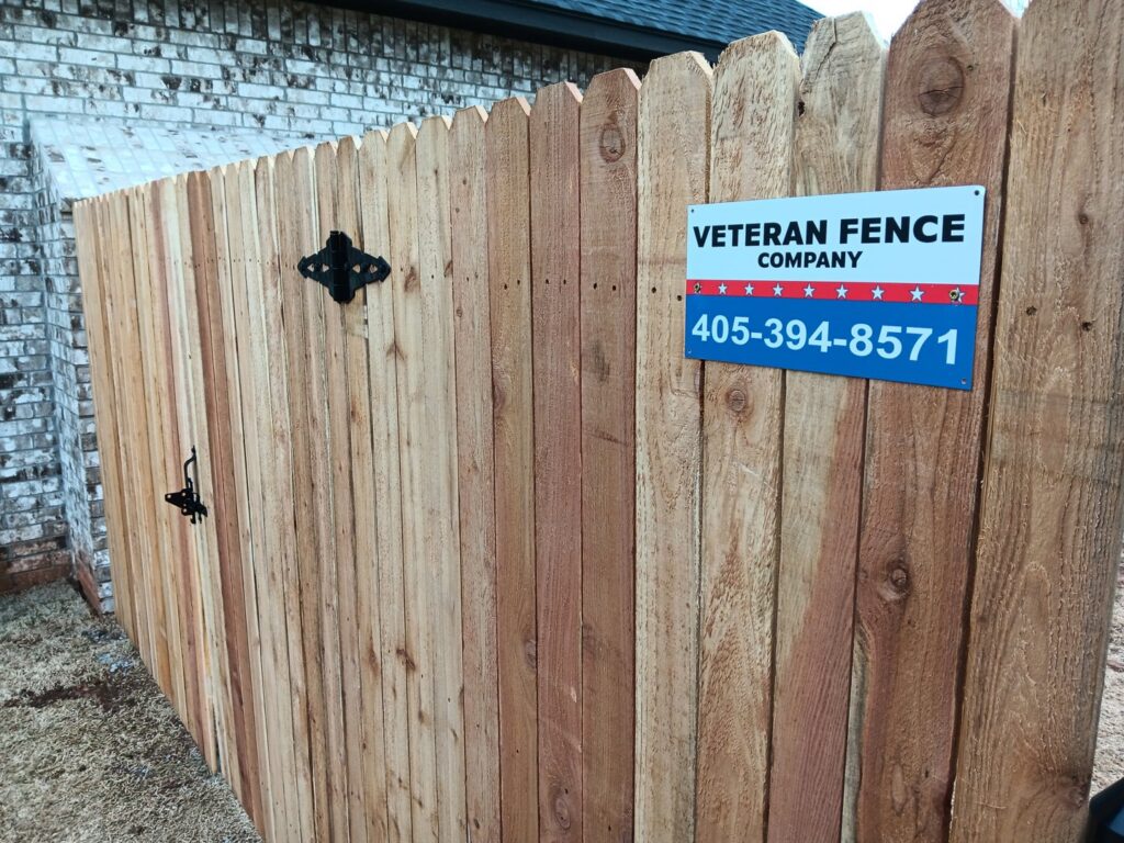 A new wood privacy fence with a gate and company sign installed by Veteran Fence Company LLC in Shawnee, OK.