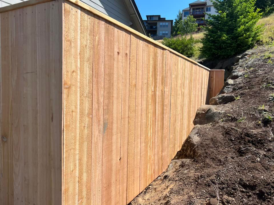 A newly installed wood privacy fence on a sloped property by RL Quality construction in Gaston, OR.