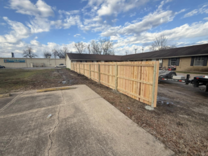 A newly installed wood privacy fence by Swanson Fencing in Jonesboro, AR, separating a parking lot from residential buildings.