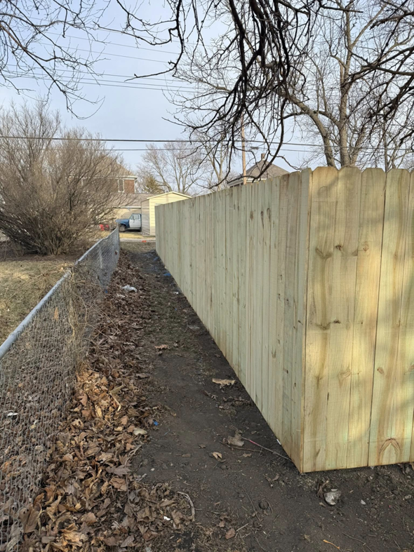 A new wood privacy fence installed by Heath's Outdoor Services LLC in Champaign, IL, next to an existing chain-link fence.