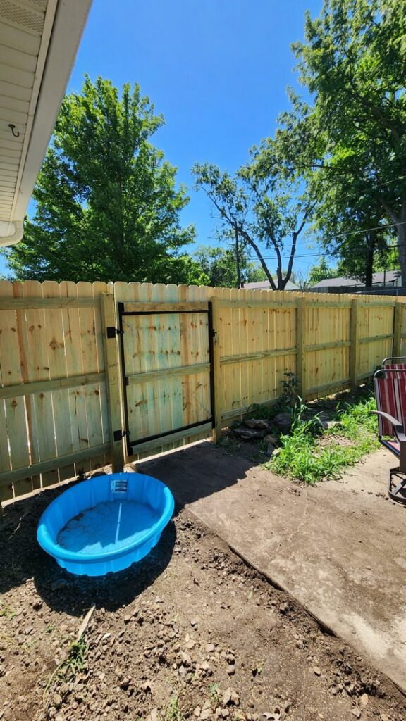 A newly installed wood privacy fence with a gate next to a residential home by Hotshot Fencing and Gates in Kansas City, MO.