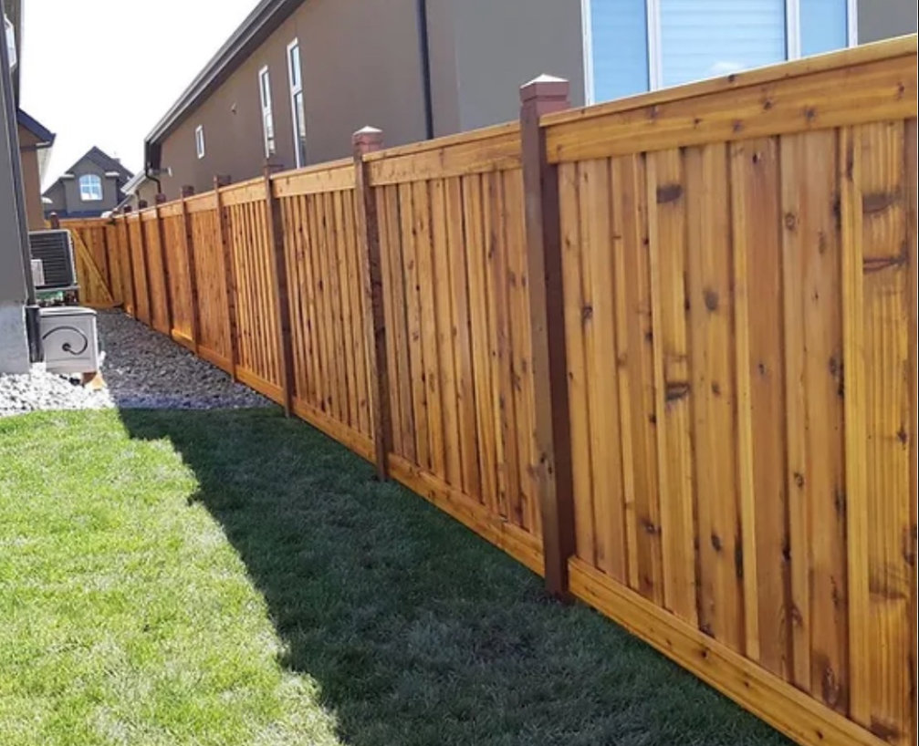 A newly installed wood privacy fence with decorative post caps bordering a green lawn by R&S Fencing & Design LLC in Denver, CO.