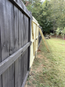 A close-up view of a new wooden fence section being installed next to an existing dark fence by Myers & Dunlap Fence Repair in Greenville, SC.