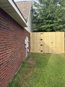 A newly installed wooden privacy fence with a matching gate next to a brick house by Riggins Renovations LLC in Biloxi, MS.