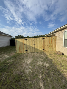 A newly installed wooden privacy fence with decorative hinges in a residential backyard by Littleton Construction LLC in the Service Area.
