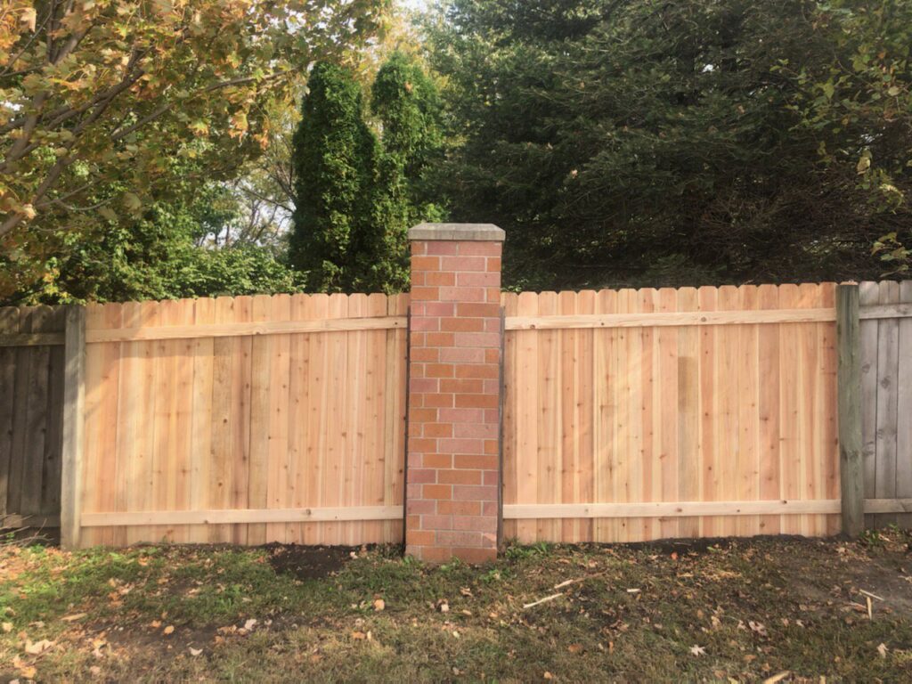 A newly installed wooden privacy fence with a decorative brick pillar by Stallworth Home Improvement in Des Moines, IA.