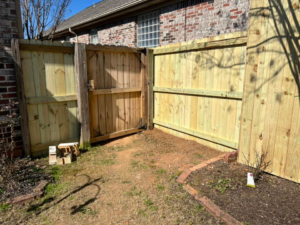 A newly installed wooden privacy fence with a gate next to a brick house by Allen Fences & Decks, LLC in Tuscaloosa, AL.