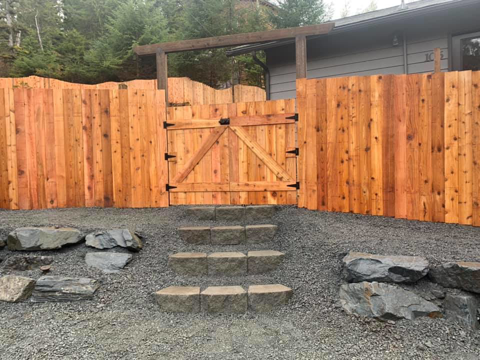 A newly installed wooden privacy fence with a matching gate, expertly crafted by Baranof Landscaping in Sitka, AK.