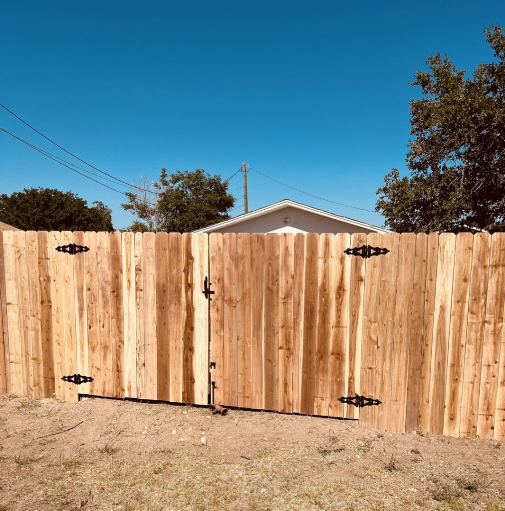 A newly installed wooden privacy fence with a gate and decorative black hinges, built by DC Fencing LLC in Clovis, NM.