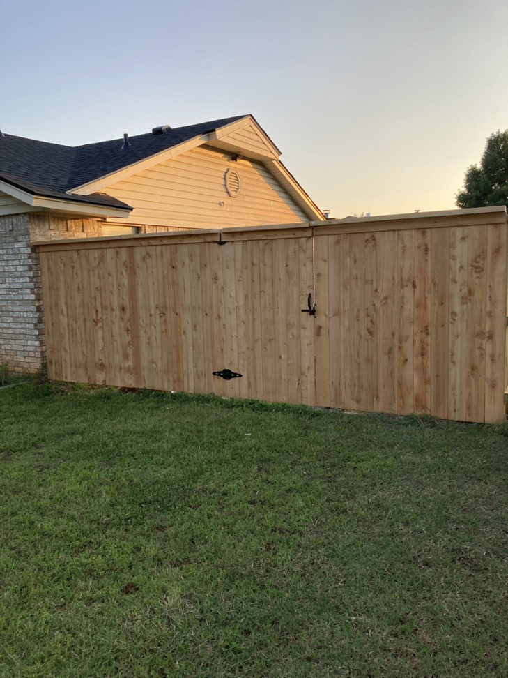 A newly installed wooden privacy fence with a gate in a residential backyard by TOP TIER FENCE LLC in Oklahoma City, OK.