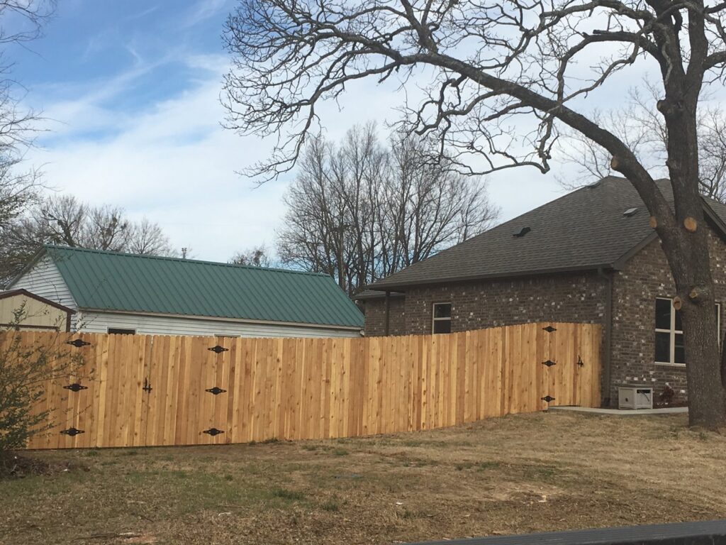 A newly installed wooden privacy fence with decorative gates enclosing a backyard by D-Fence of Tulsa in Tulsa, OK.
