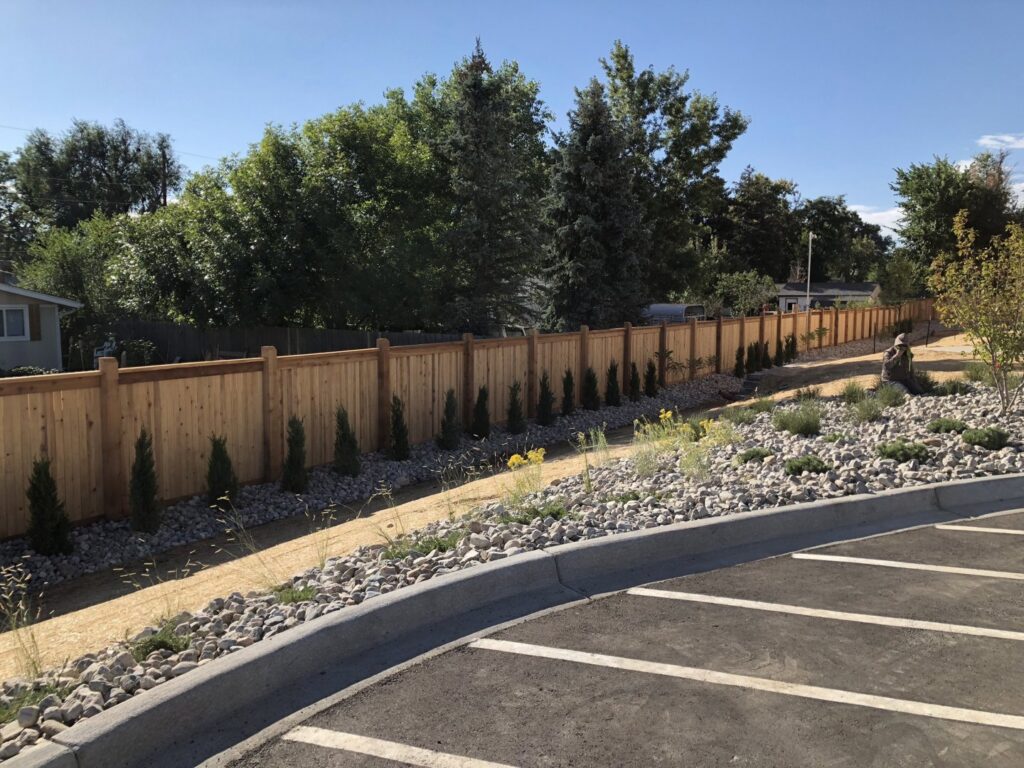 A long, newly installed wooden privacy fence bordering a parking lot, completed by First Rate Fence & Supply in Denver, CO.