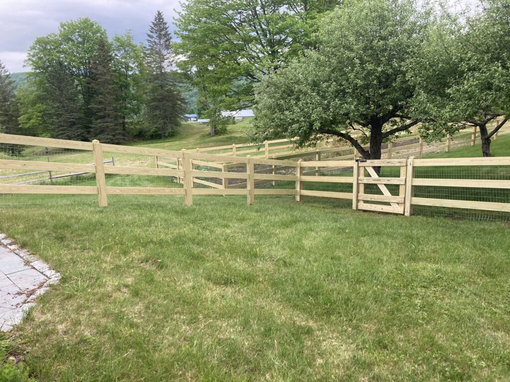 A newly installed wooden rail fence with a matching gate in a green grassy yard by Doolan Fence in Montpelier, VT.