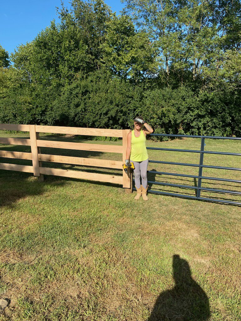 A newly installed wooden rail fence and metal gate by Stapleton Fencing LLC in Lexington, KY, with a worker standing nearby.