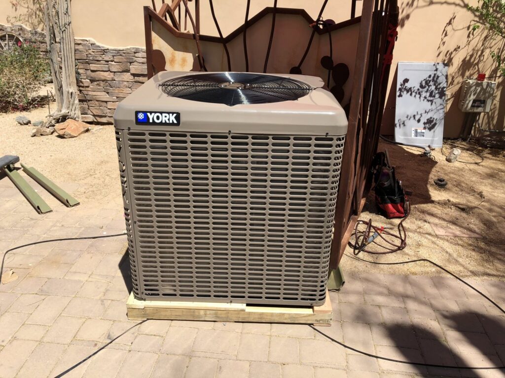 A newly installed York brand outdoor AC condenser unit on a wooden pad by Hellerud Air in Peoria, AZ.