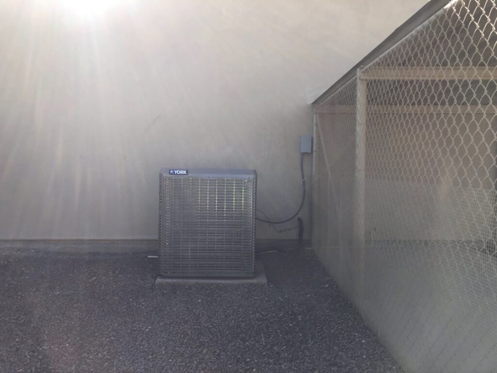 A newly installed York brand outdoor AC condenser unit next to a building wall by Hellerud Air in Peoria, AZ.
