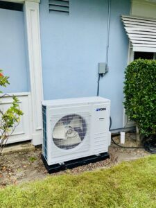A newly installed York brand outdoor HVAC condenser unit next to a blue house by Pelican Heating and Air in Carlsbad, CA.