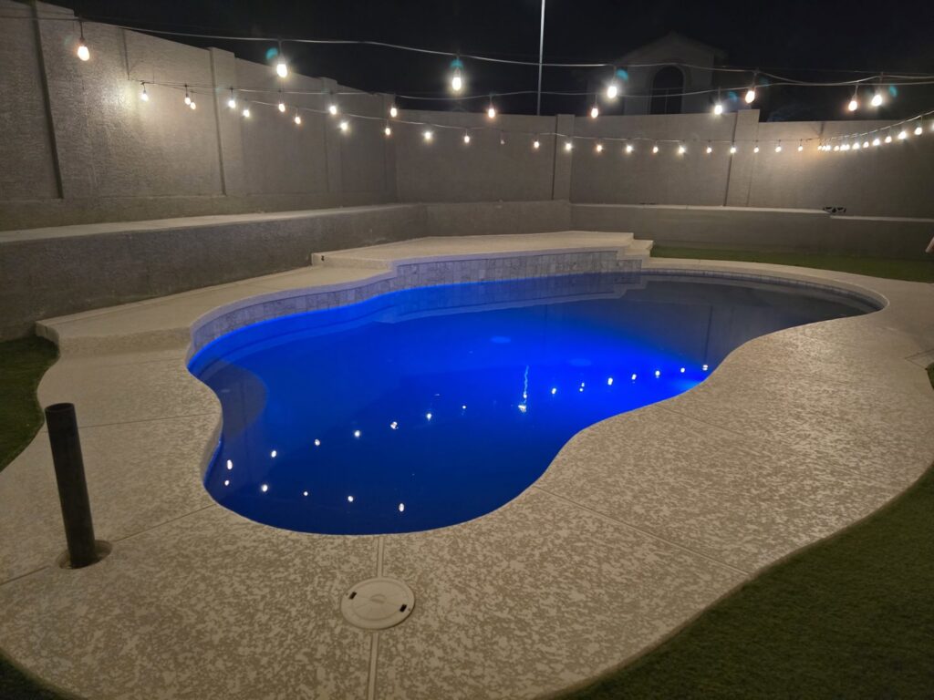 A newly built swimming pool with vibrant blue lighting and overhead string lights by All Valley Pools in Avondale, AZ.