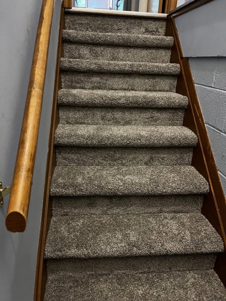A newly carpeted staircase with brown carpet installed by Carpet Warehouse Lorain LLC in Lorain, OH.