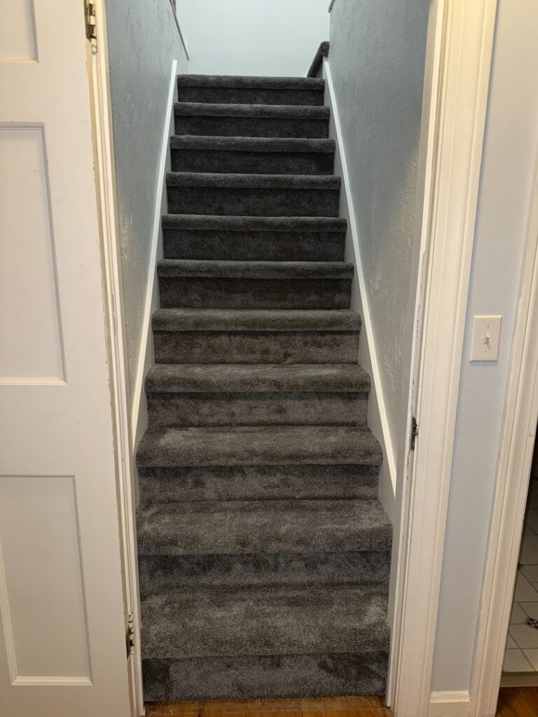 A newly carpeted staircase with gray carpet installed by Carpet Warehouse Lorain LLC in Lorain, OH.