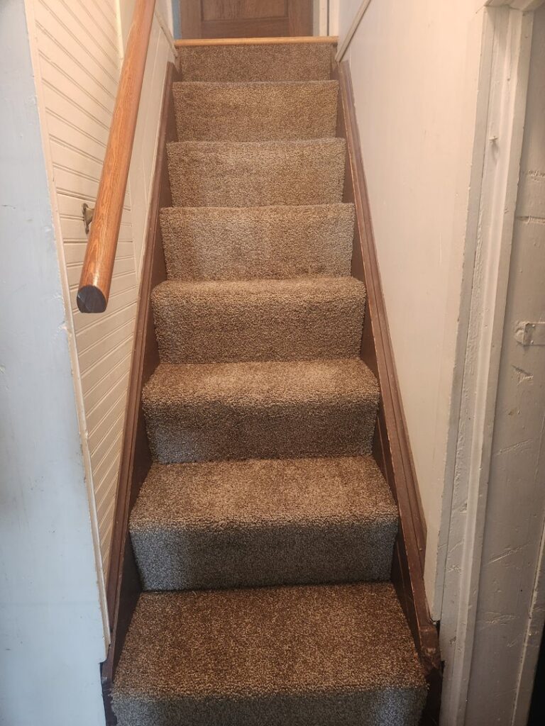 Newly carpeted stairs with a wooden handrail installed by Carpet Clearance Warehouse Pueblo, CO.
