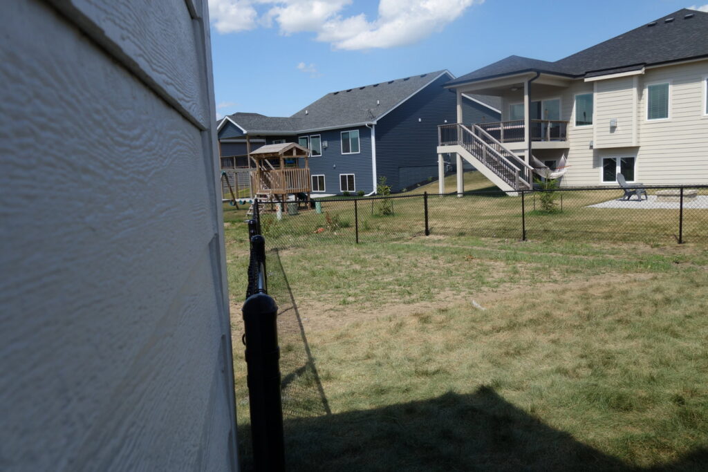 A newly installed black chain-link fence running along a residential backyard by Stallworth Home Improvement in Des Moines, IA.