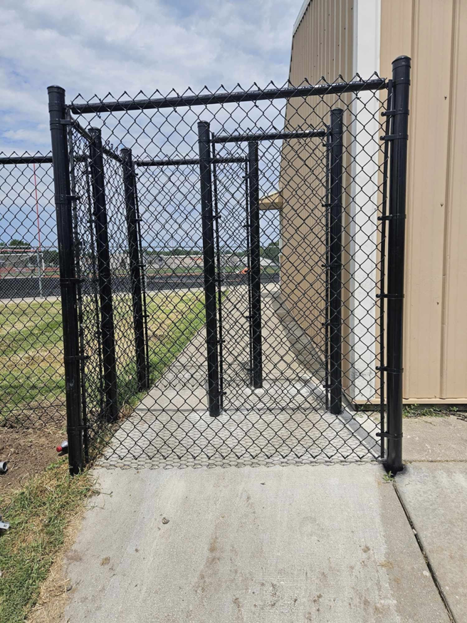 A newly installed black chain-link fence with a gate next to a commercial building by Atchison Fence in Effingham, KS.