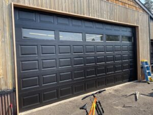 A newly installed modern black garage door with windows on a wooden building, completed by Above The Rest Garage Door in Colorado Springs, CO.