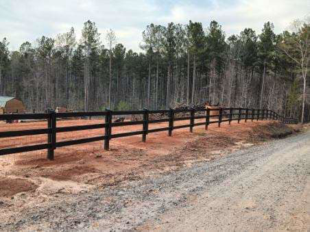 A newly installed black wooden farm fence along a dirt road by Almaraz & Sons LLC in Macon, GA.