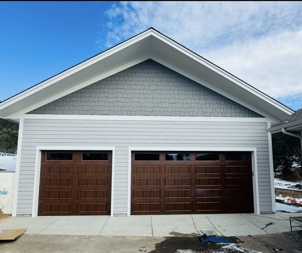 A residential house featuring two newly installed brown panel garage doors by PNG Garage Doors llc in Lakewood, CO.