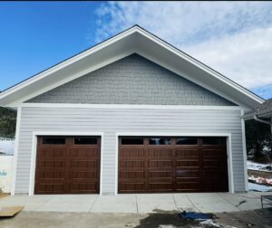 A residential house featuring two newly installed brown panel garage doors by PNG Garage Doors llc in Lakewood, CO.