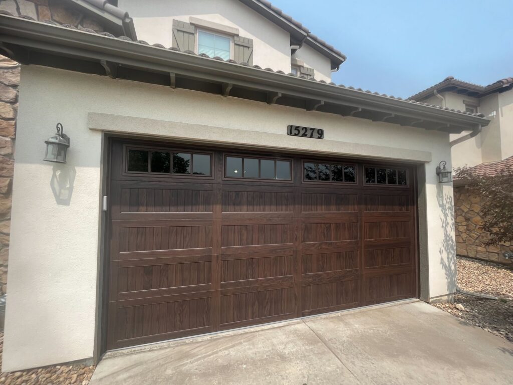 A residential house featuring a newly installed dark brown garage door with top windows by PNG Garage Doors llc in Lakewood, CO.