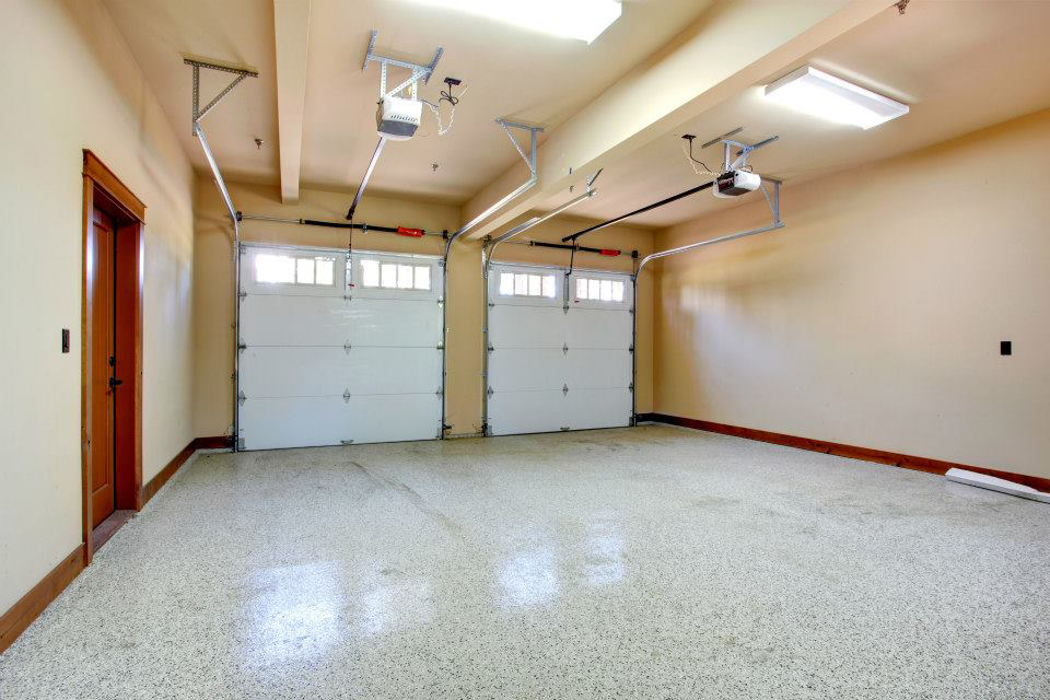 Interior view of a garage with two newly installed white garage doors and openers by Integrity Garage Door Repair in Clearwater, FL.