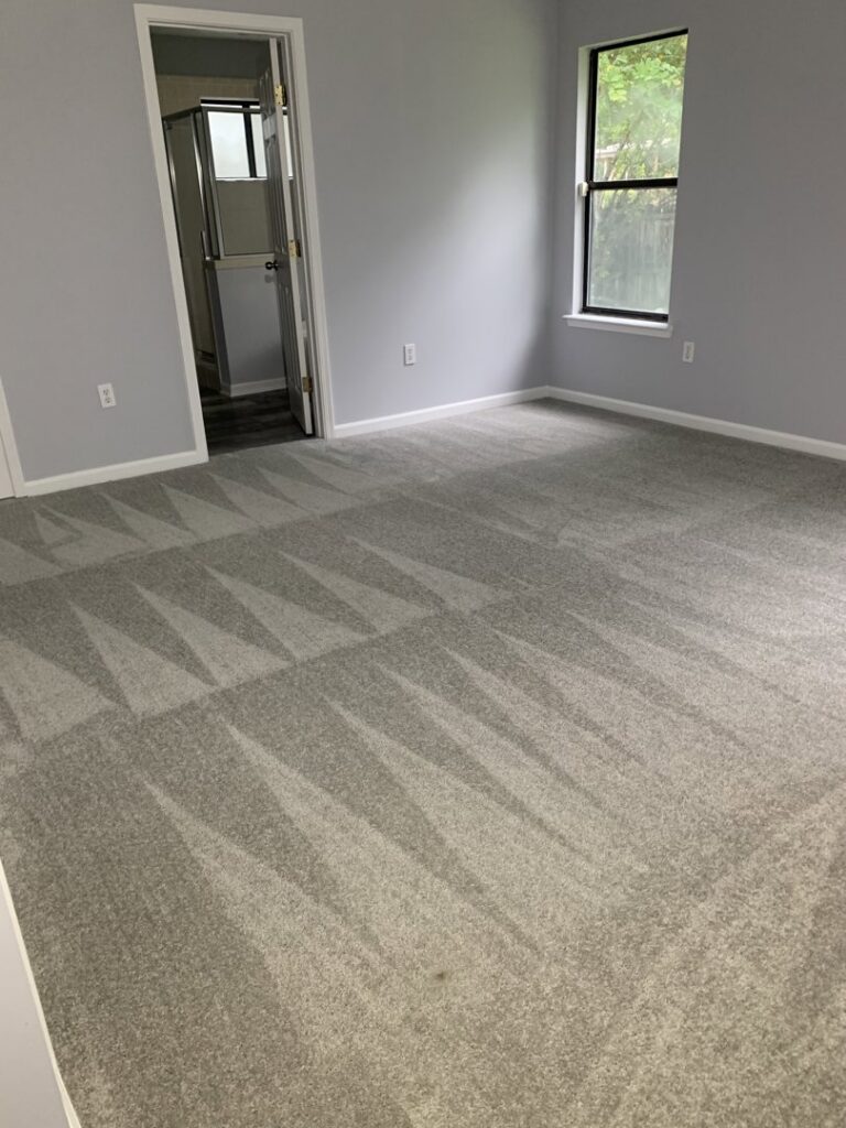 A bedroom featuring newly installed grey carpet with visible vacuum lines, completed by Gator Carpet and Tile in Jacksonville, FL.