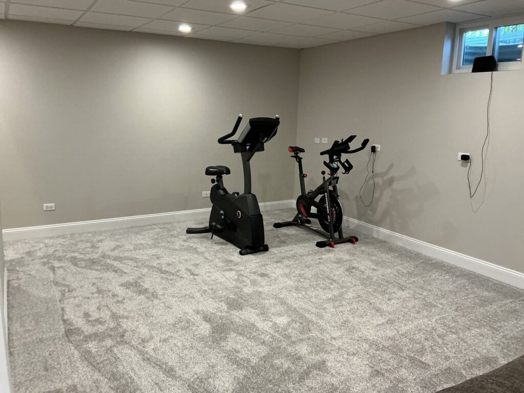 A home gym with newly installed light grey carpet, showcasing a completed job by At Home Flooring in Naperville, IL.