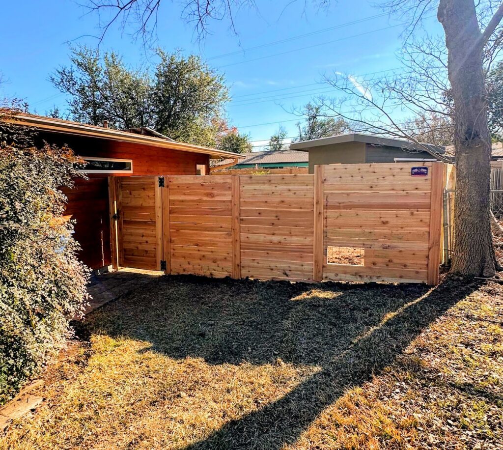 A newly installed horizontal wood fence featuring a convenient pet door, built by Stand Strong Fencing of East Austin, TX.