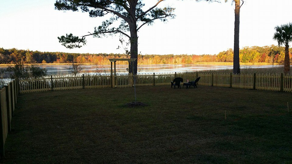 A newly installed light-colored wooden picket fence enclosing a backyard by Lowcountry Home Works843 LLC in Summerville, SC.