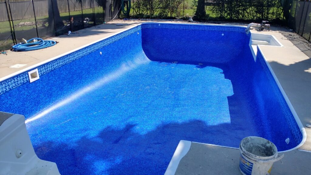 An empty pool with a newly installed blue liner and a bucket on the deck, showcasing work by Brian's Pool Service in Baton Rouge, LA.
