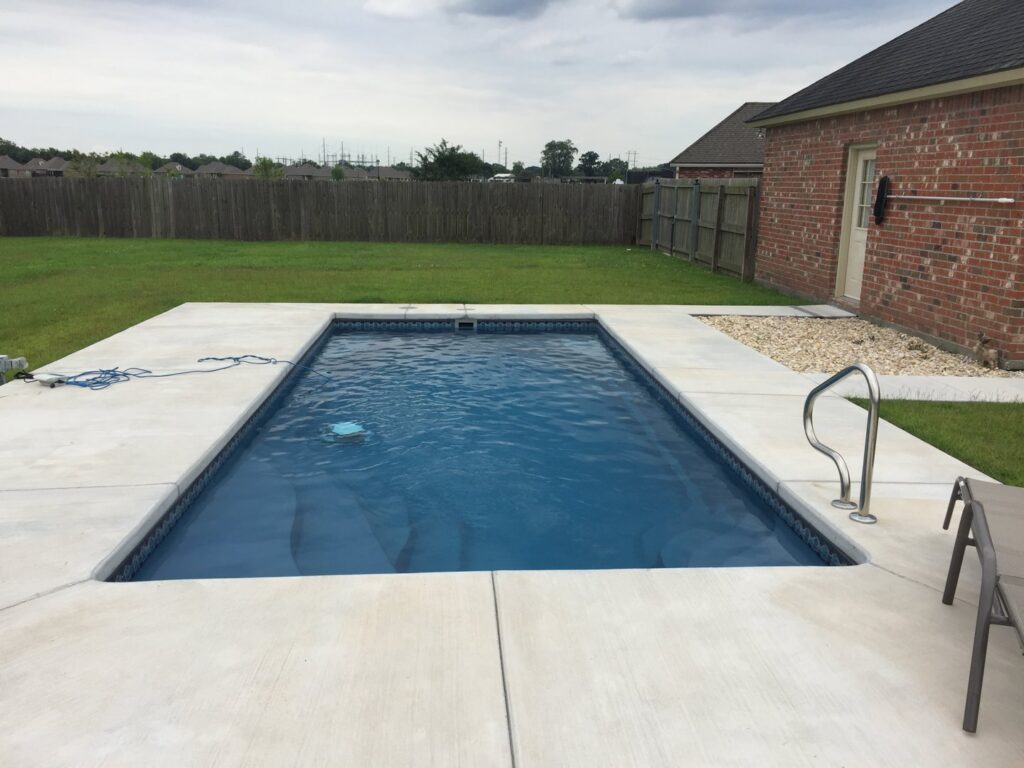 A newly installed rectangular swimming pool with clean concrete decking by Central Pools, Inc. in Baton Rouge, LA