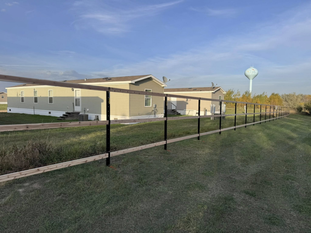 A newly installed two-rail fence with black posts and wooden rails by Nailed It Fencing in Williston, ND.