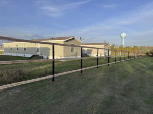 A newly installed two-rail fence with black posts and wooden rails by Nailed It Fencing in Williston, ND.